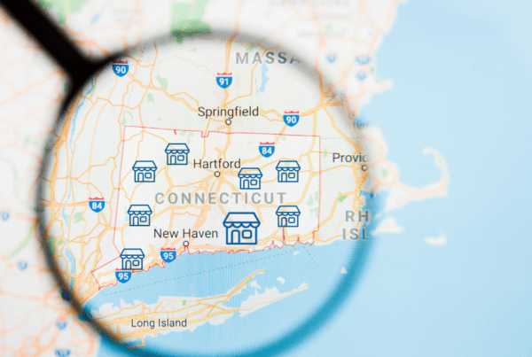 Magnifying glass over a map of Connecticut highlighting V.F. McNeil Insurance helping businesses across the state with commercial liability and risk protection.
