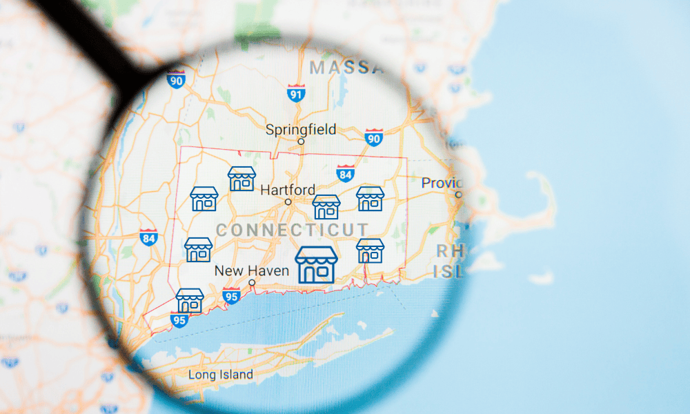 Magnifying glass over a map of Connecticut highlighting V.F. McNeil Insurance helping businesses across the state with commercial liability and risk protection.