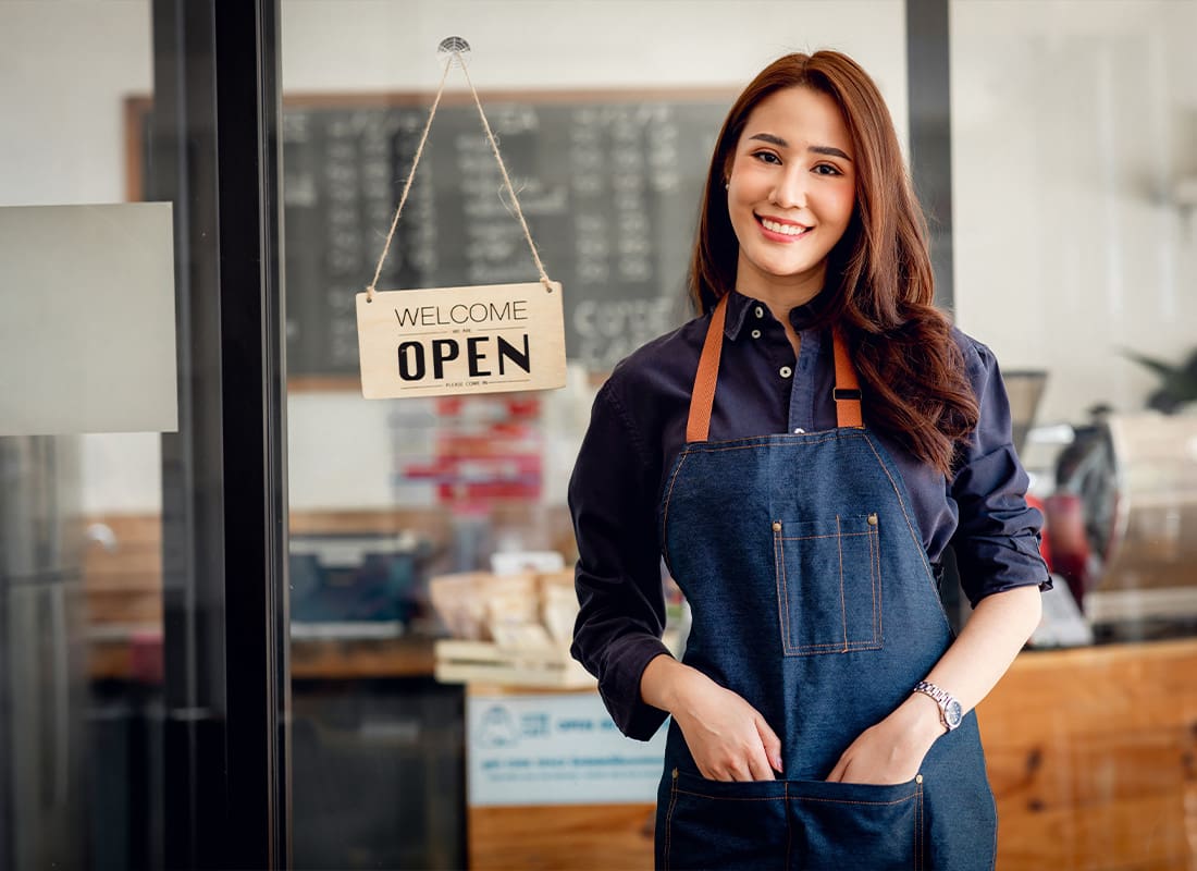 Insurance by Industry-Small-Business-Owner-at-Entrance-Looking-at-Camera-in-an-Apron