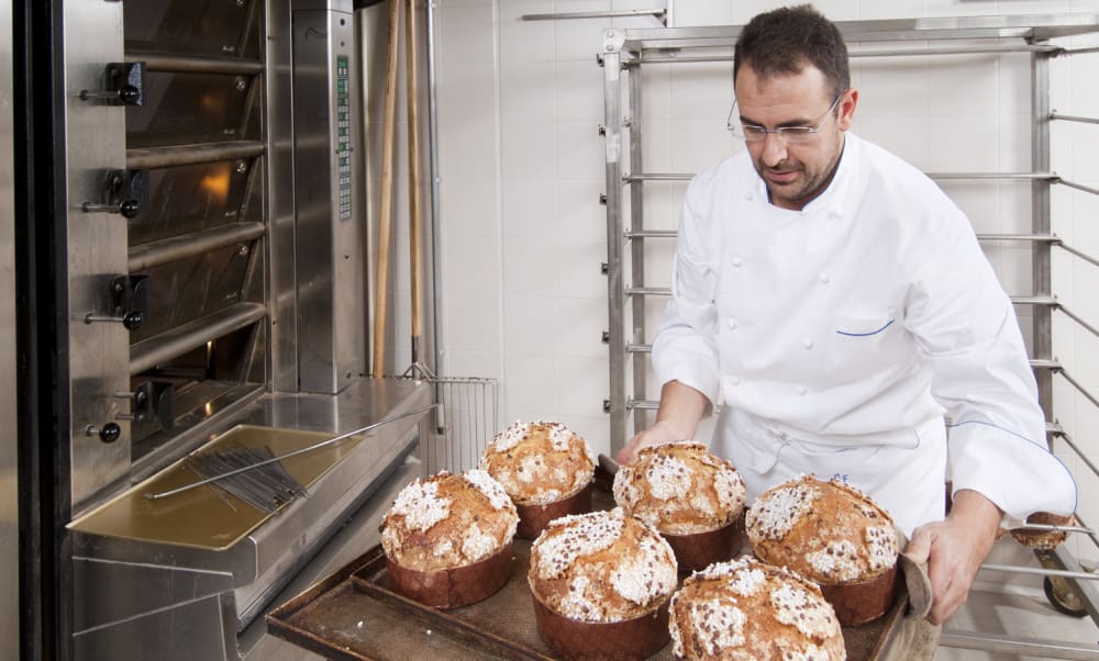 Common Risks Faced By Connecticut Bakeries. Male baker taking trays of bread out of hot oven.