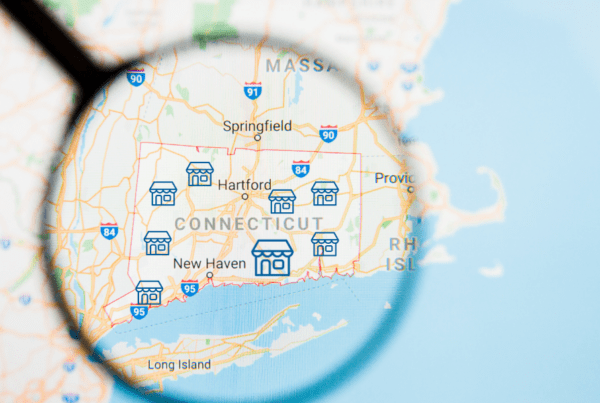 Magnifying glass over a map of Connecticut highlighting V.F. McNeil Insurance helping businesses across the state with commercial liability and risk protection.